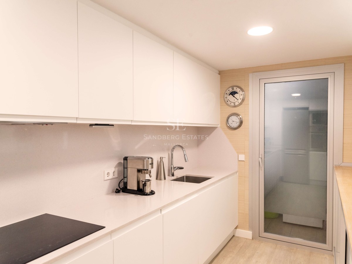 Cuisine moderne blanche avec placards sans poignées, plan de travail en quartz et porte vitrée.