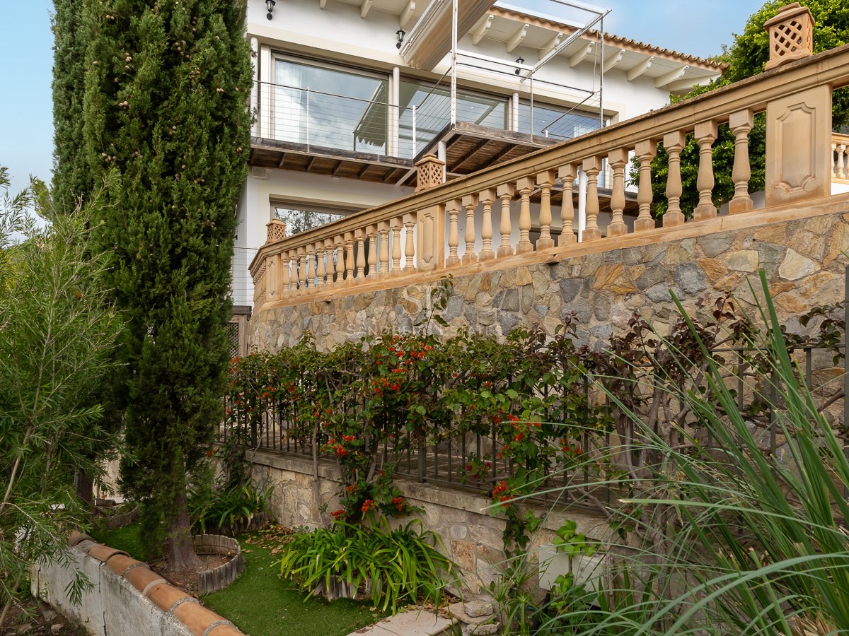 Tiered garden with stone retaining walls, classic balustrades, and lush cypress trees leading to a white villa.