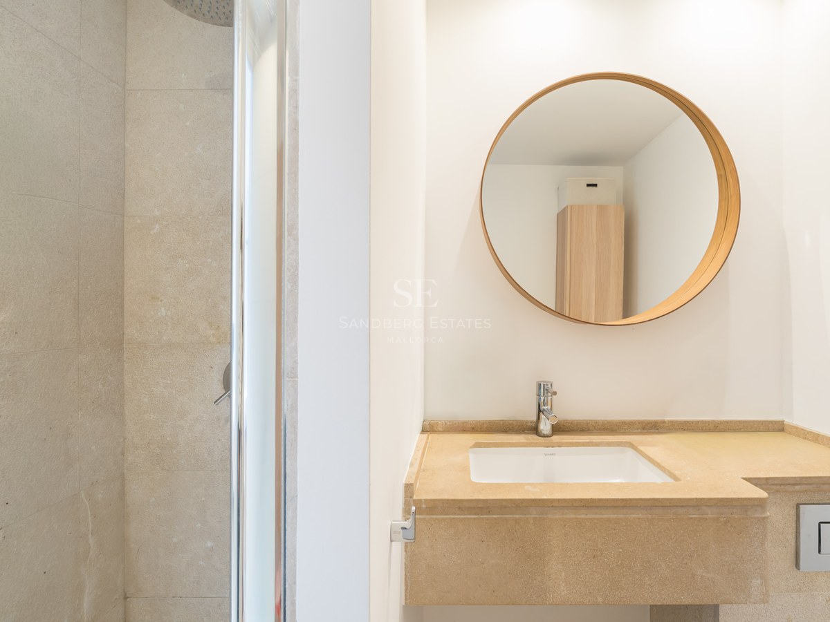 Contemporary bathroom featuring a beige stone vanity, round wooden mirror, and a glass walk-in shower.