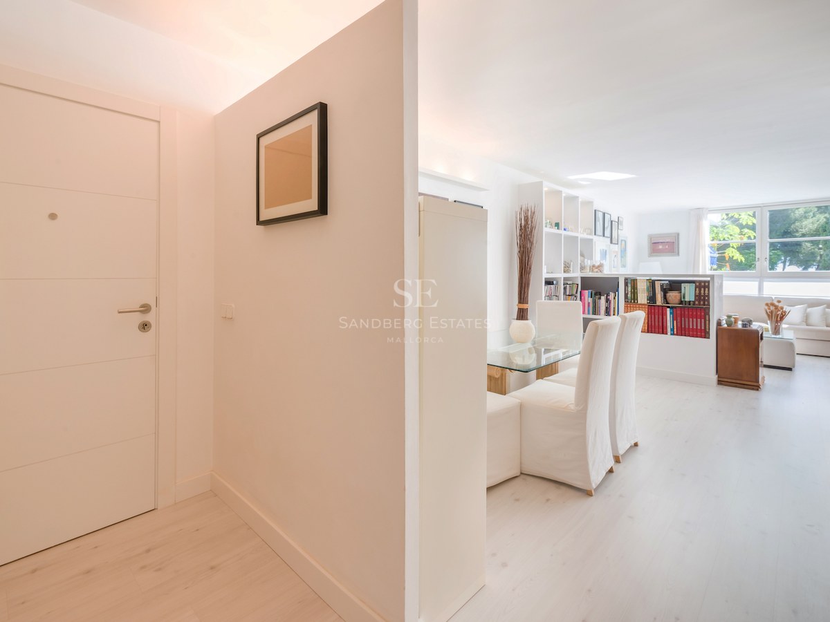 Une entrée blanche et lumineuse menant à un salon minimaliste avec du parquet en bois clair et de grandes fenêtres.