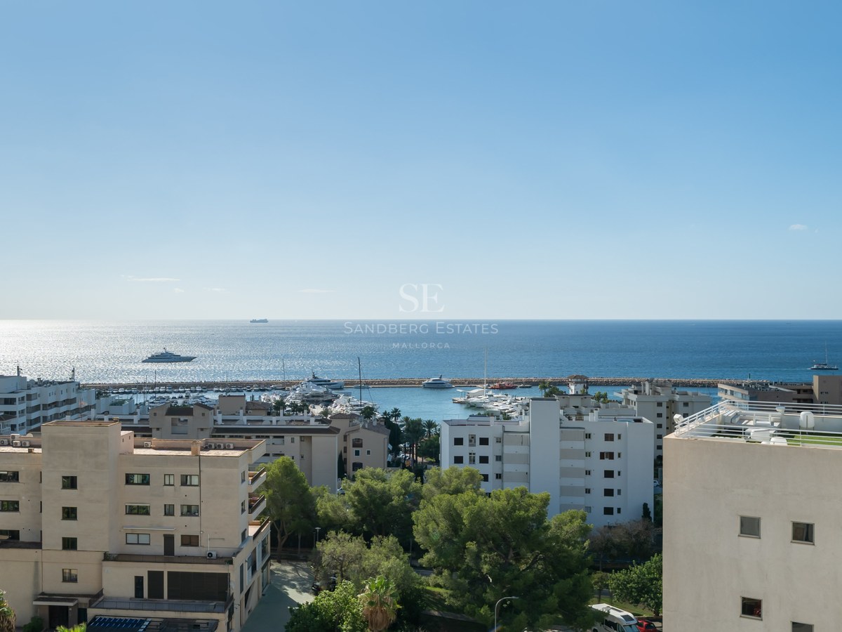 Vue en hauteur d'une ville côtière, d'un port rempli de yachts et de la mer Méditerranée sous un ciel bleu.