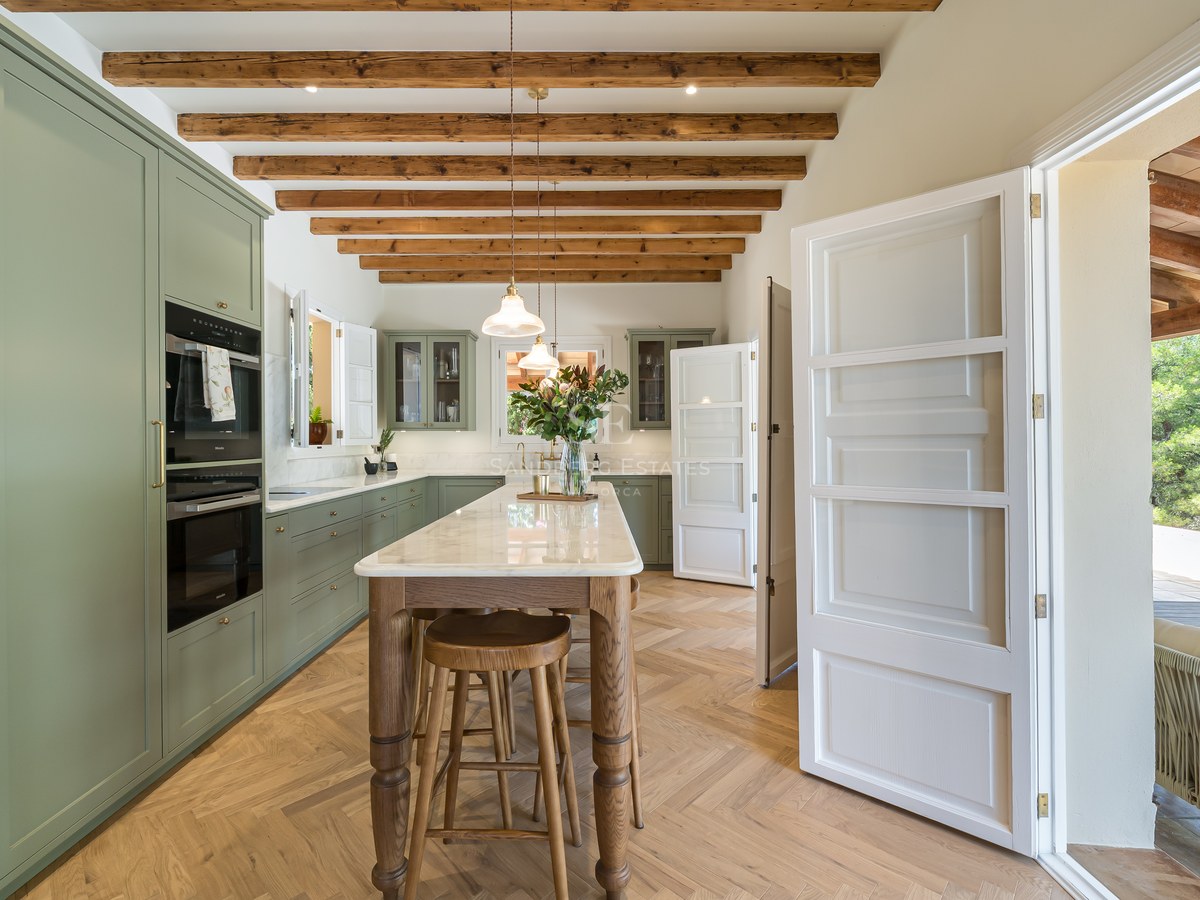 Luxury kitchen featuring sage green cabinets, marble-topped island, herringbone wood floors, and rustic ceiling beams.