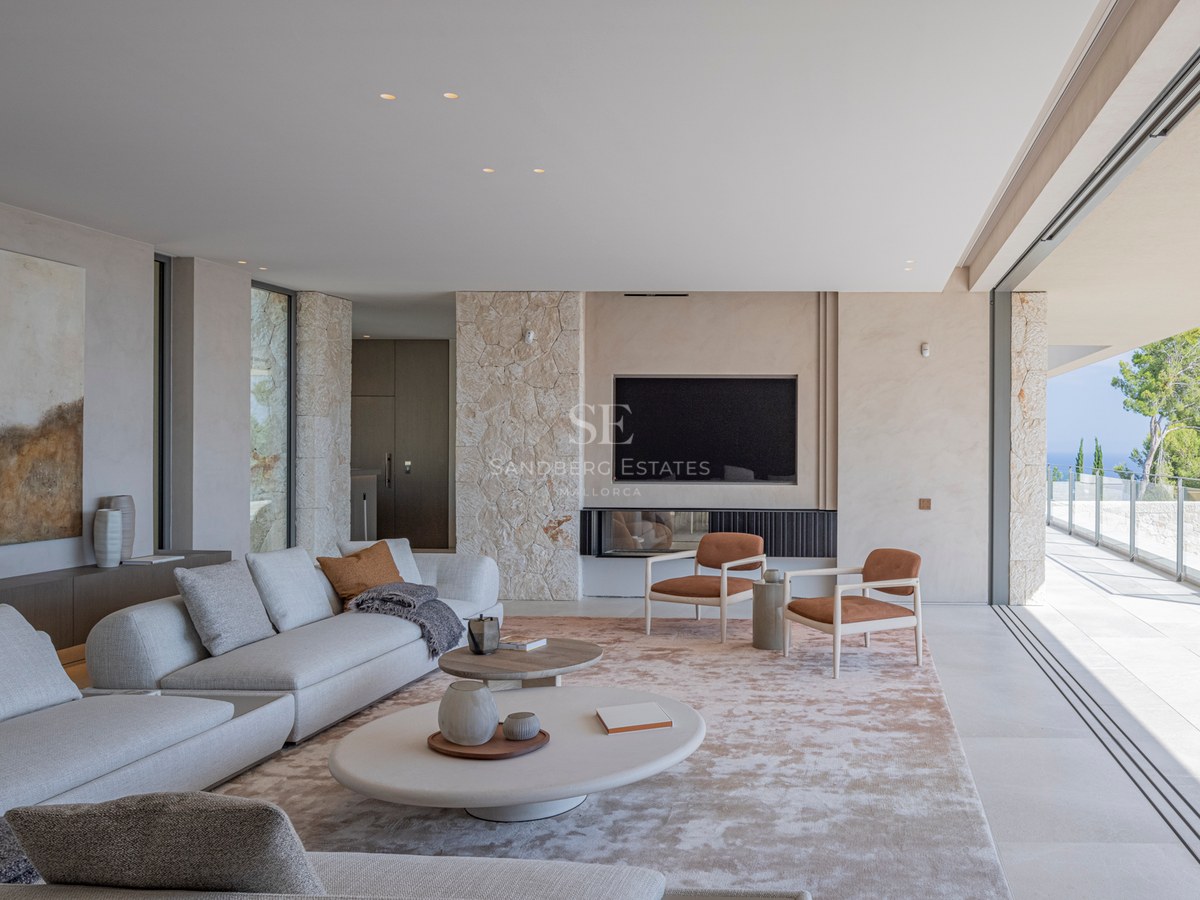 Salon minimaliste avec murs en pierre, canapé gris et baies vitrées coulissantes ouvrant sur une terrasse.