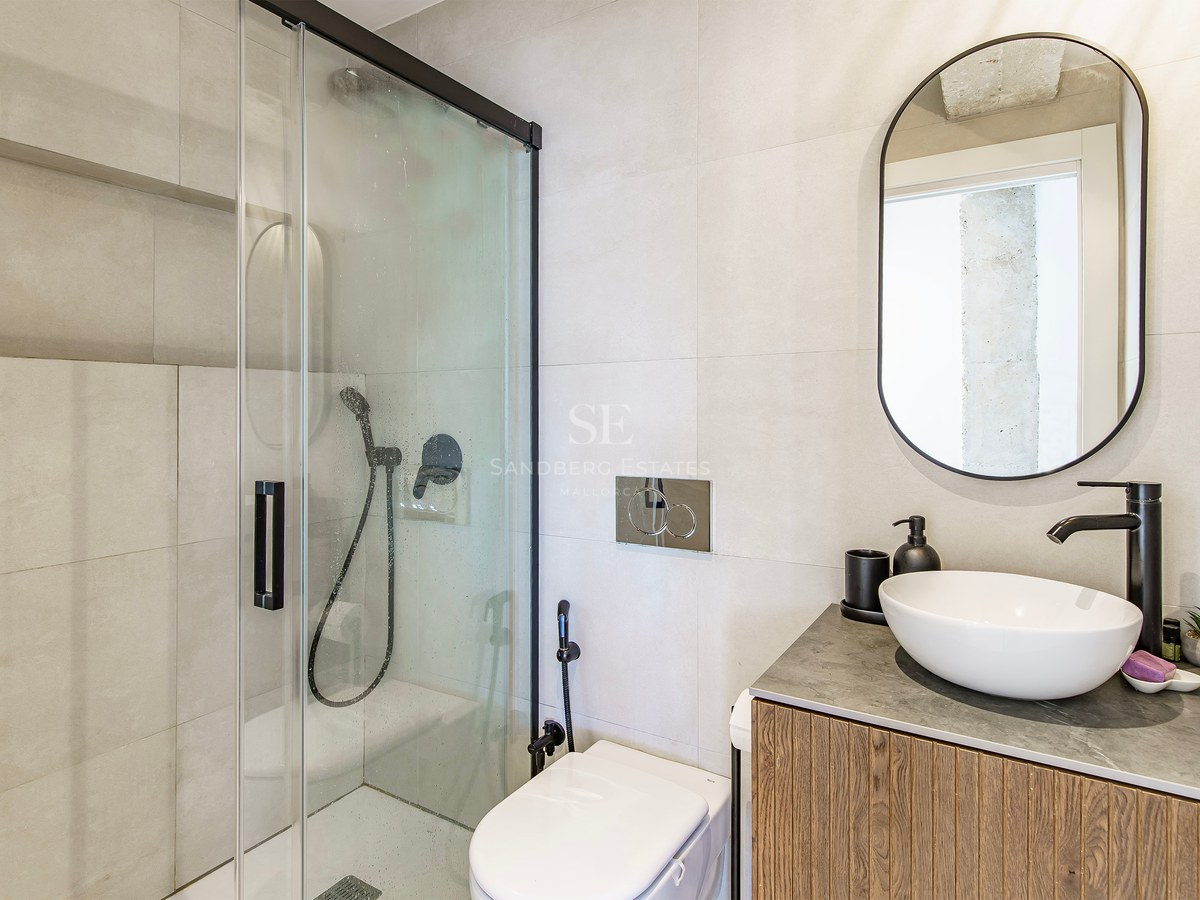 Salle de bain contemporaine avec douche vitrée, robinetterie noire, meuble en bois et miroir ovale.