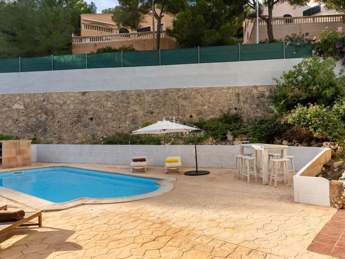 Private swimming pool with lounge chairs, white umbrella, and a rustic stone wall background.
