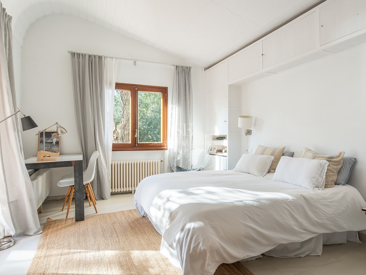 Dormitorio luminoso con cama blanca, techos altos abovedados, alfombra de fibras naturales y un escritorio junto a la ventana.