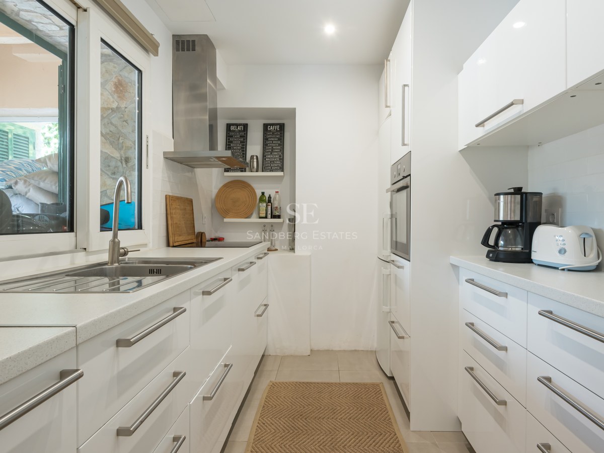 Cuisine lumineuse avec placards blancs brillants, plans de travail en quartz et appareils en inox.