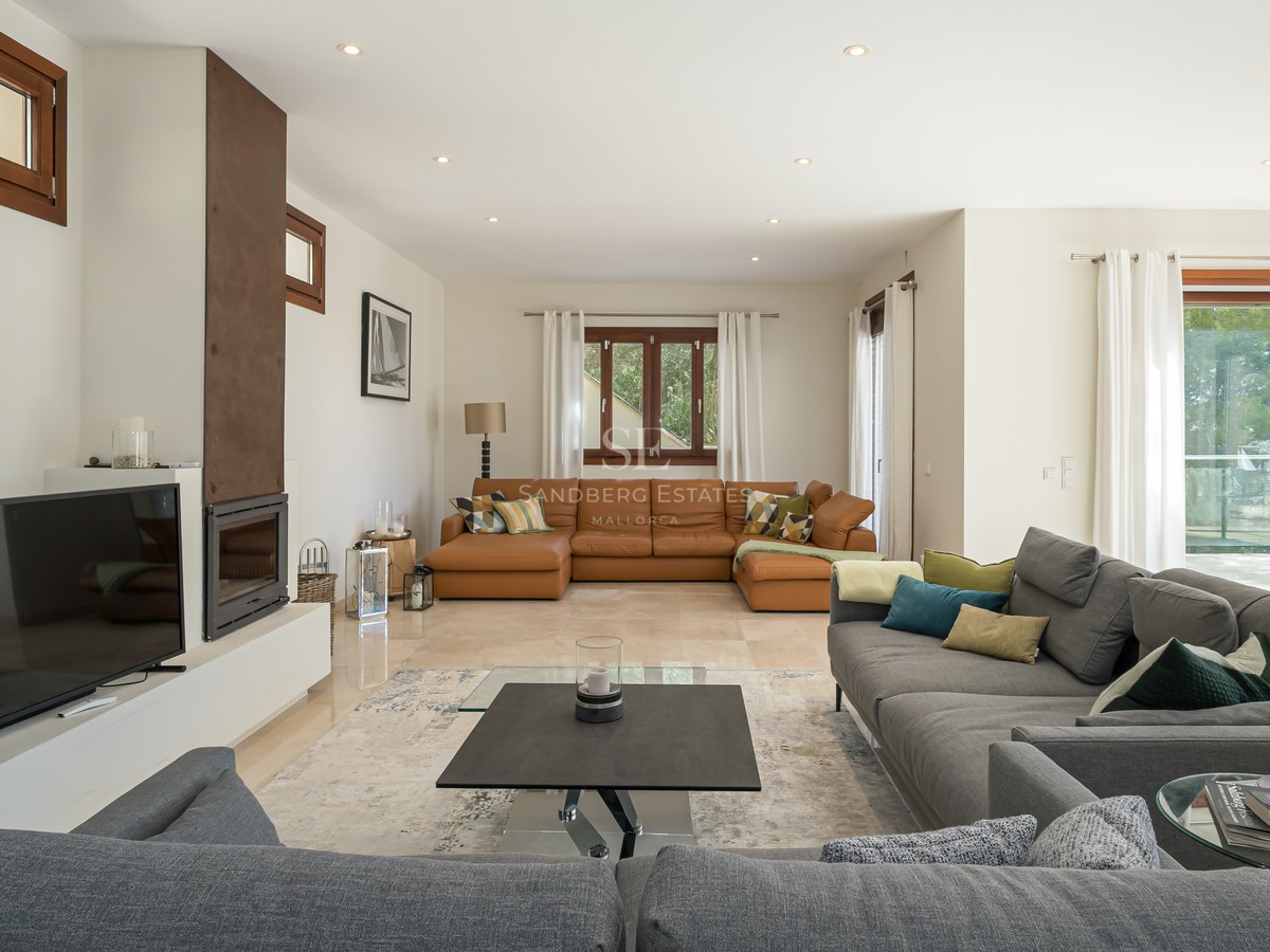 Salón amplio con sofás en gris y cuero, suelo de mármol, chimenea integrada y acceso a terraza.