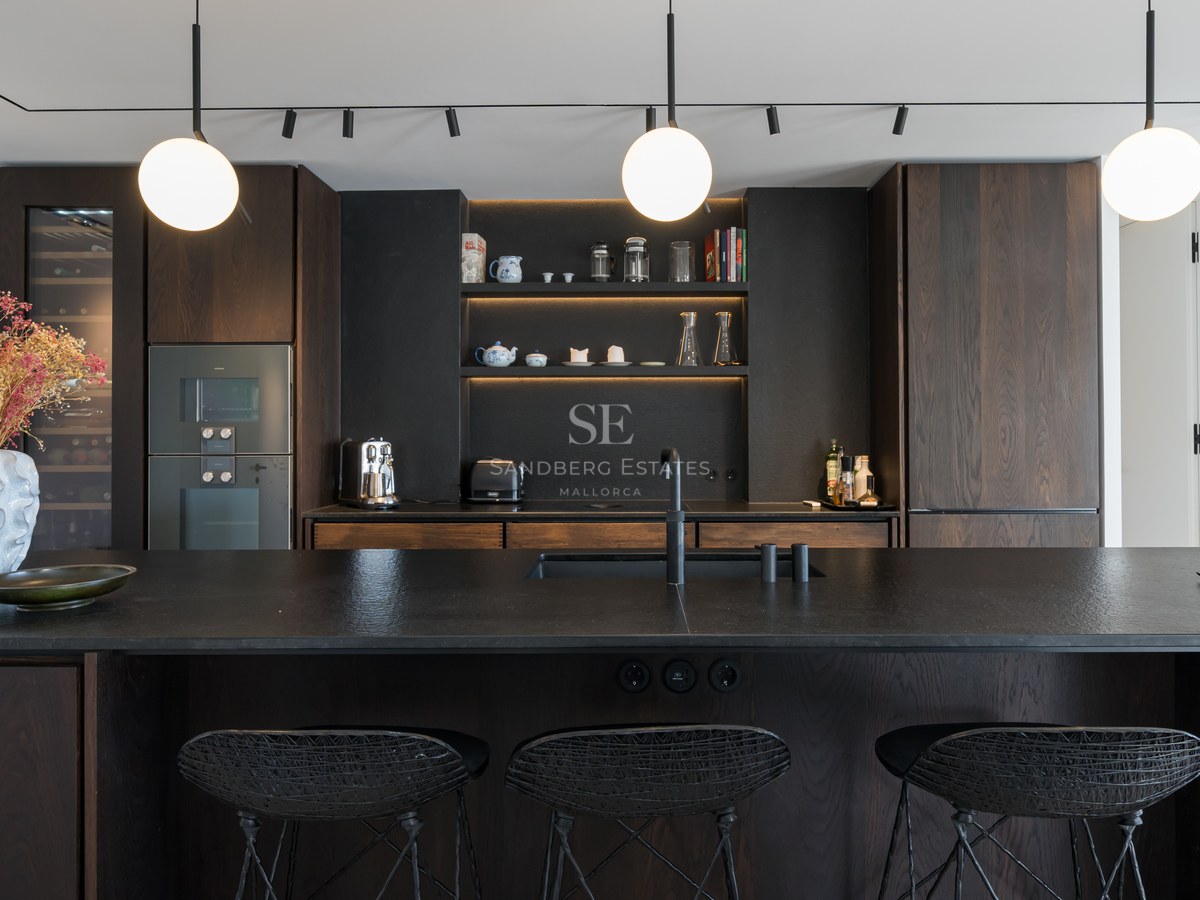 Cuisine moderne avec placards en bois sombre, îlot noir texturé avec tabourets et suspensions sphériques.