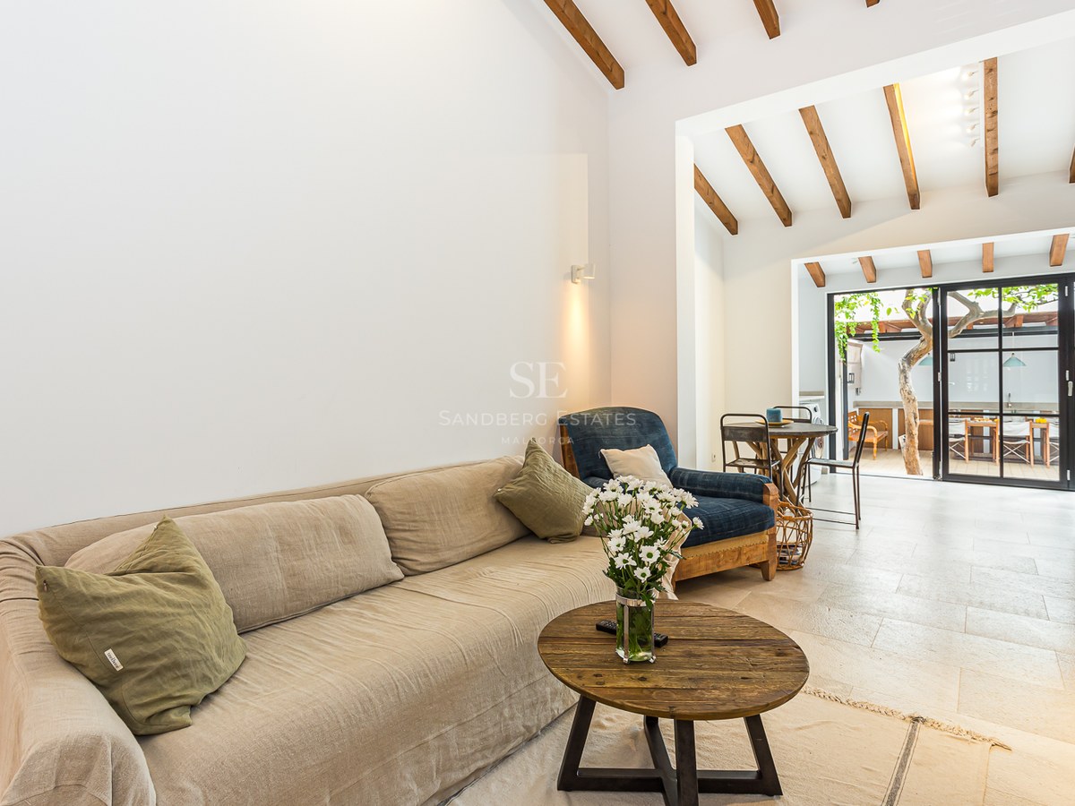 Salón con sofá beige, mesa de centro de madera, vigas expuestas y puertas de cristal que dan al patio.