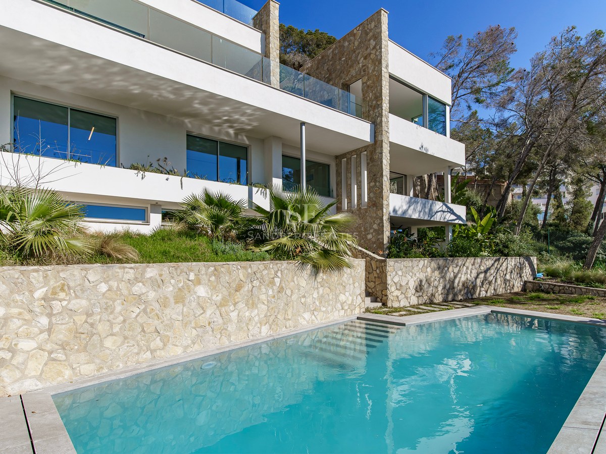 Villa moderne à plusieurs niveaux avec piscine turquoise, murs en pierre naturelle et balcons en verre.