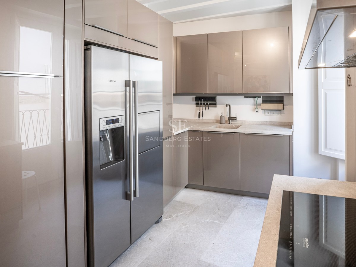 Modern kitchen with high-gloss taupe cabinets, a stainless steel side-by-side refrigerator, and light stone countertops.