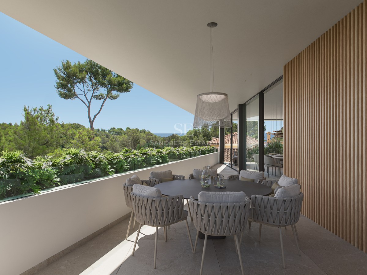 Terrasse moderne avec table ronde, chaises tressées, mur en lattes de bois et vue sur la forêt et la mer.