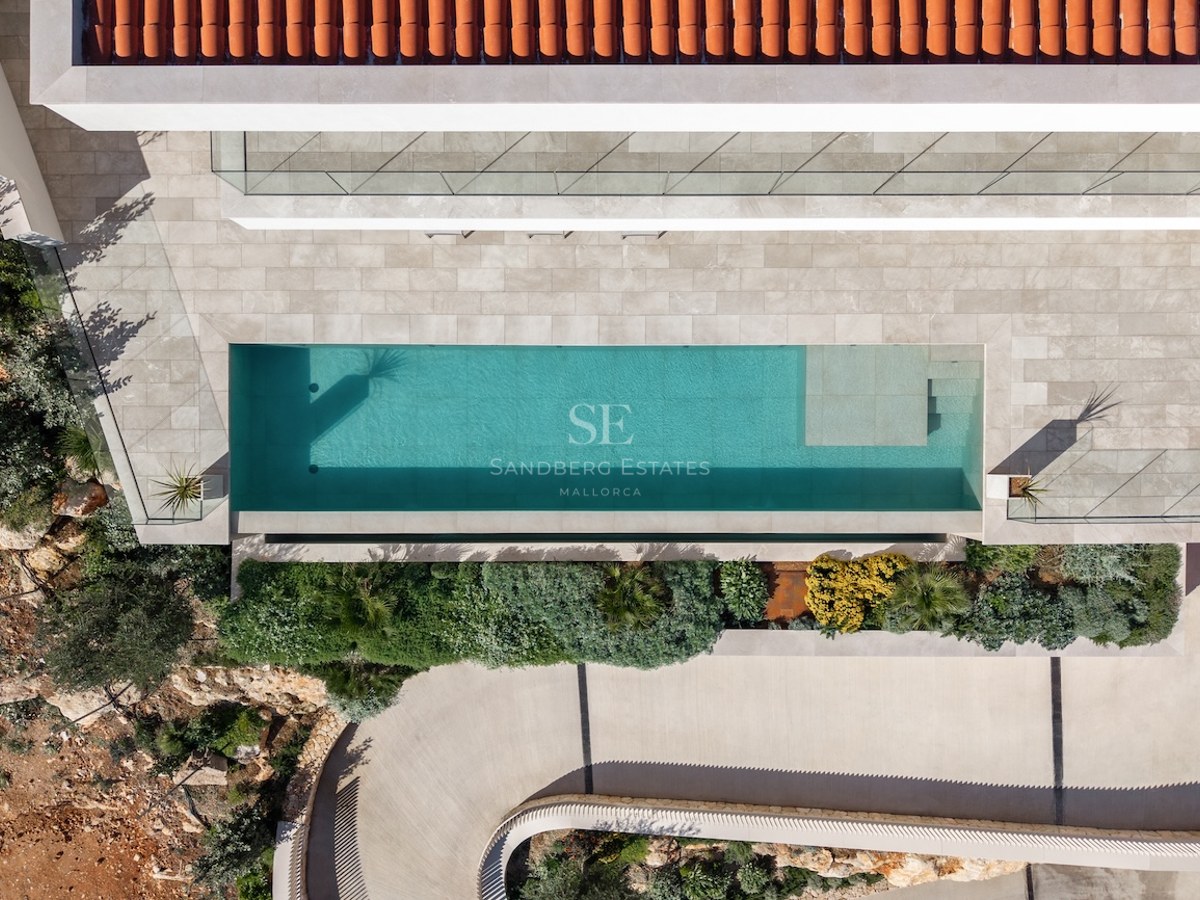 Vue plongeante d'une piscine turquoise, d'une terrasse en pierre, d'un toit en terre cuite et d'un jardin.