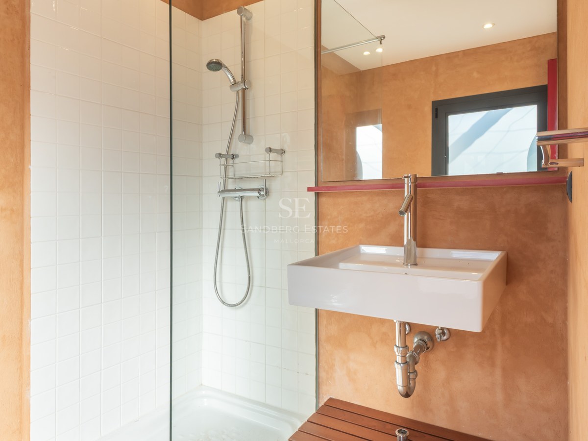 Modern bathroom featuring a walk-in glass shower, white square tiles, and warm terracotta textured walls with a white sink.