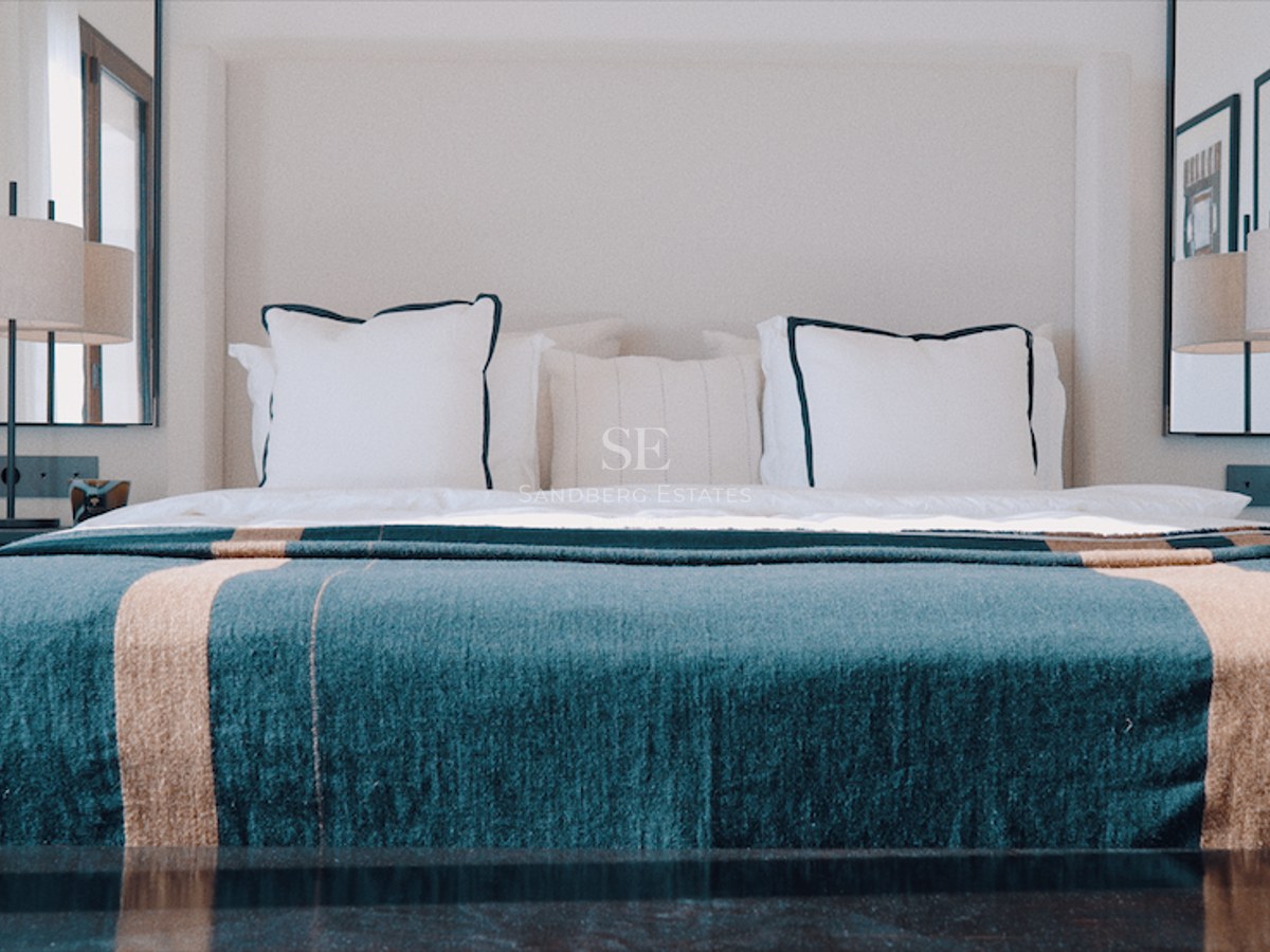 King-size bed with teal throw, symmetrical designer lamps, and wall mirrors in a luxury suite.