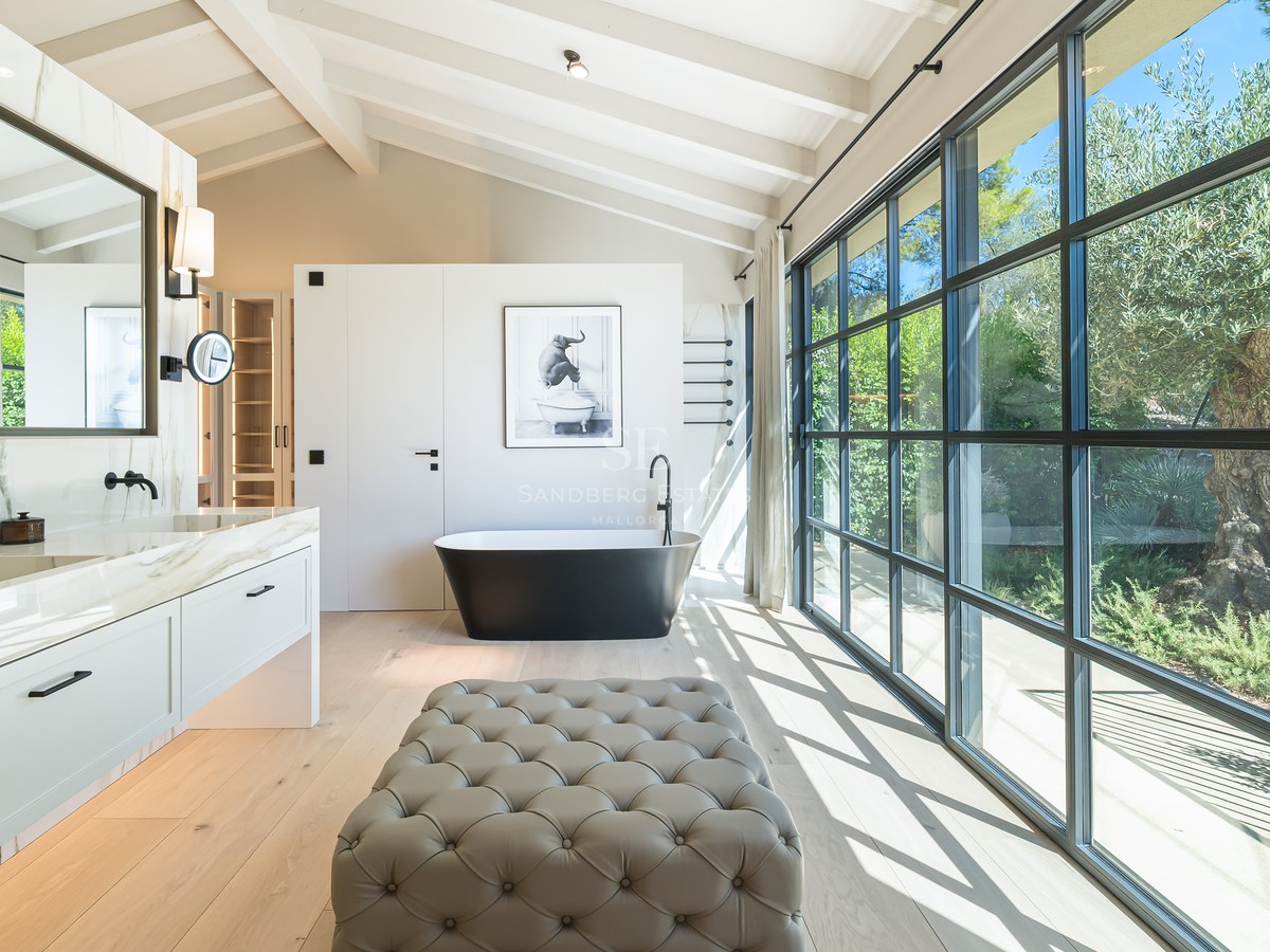 Luxury bathroom with a freestanding black tub, marble double vanity, and floor-to-ceiling windows facing a garden.