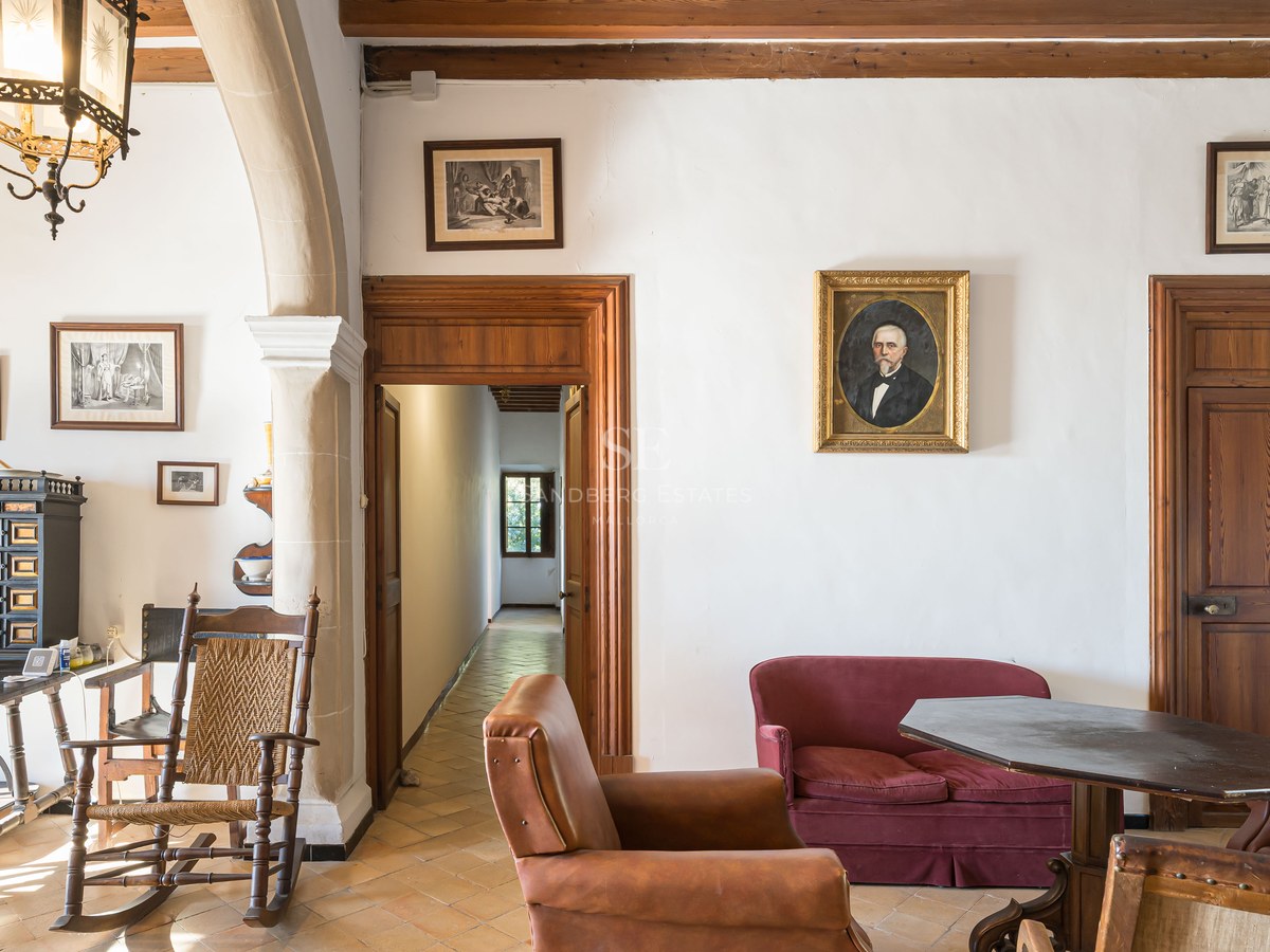 Salón clásico con muebles antiguos, suelos de terracota, sofá de terciopelo rojo y retratos en las paredes.