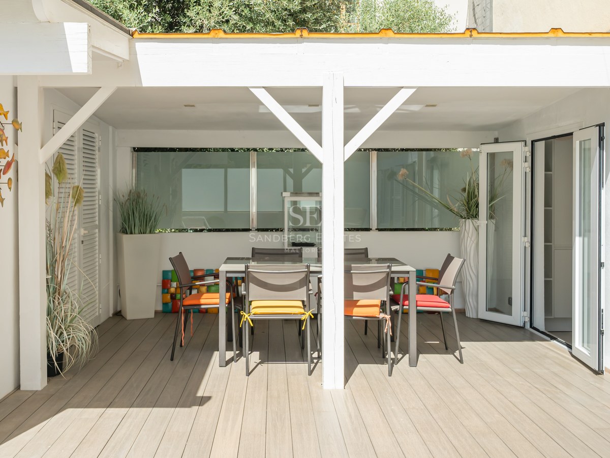 Large swimming pool lined with sun loungers, with a modern house with minimalist design in the background and lush vegetation.