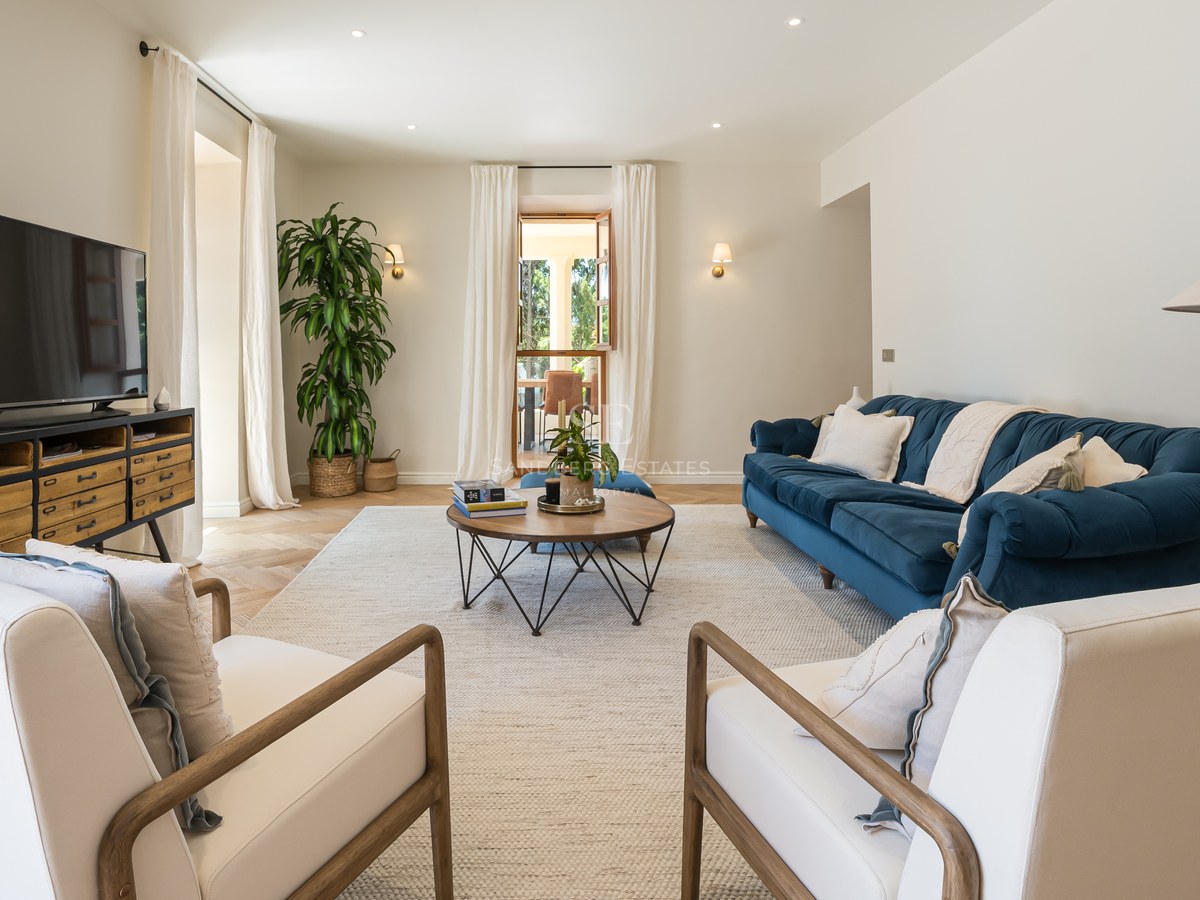 Bright living room featuring a navy velvet sofa, wooden armchairs, and chevron oak flooring leading to a terrace.