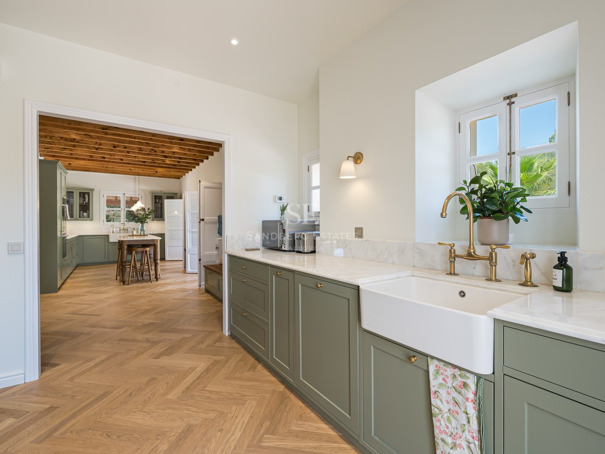 Sage green kitchen with marble countertops, brass taps, and herringbone wood flooring leading to a dining area.