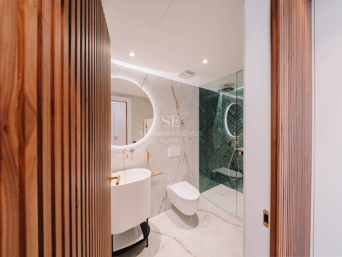 Salle de bain moderne avec marbre, miroir rond rétroéclairé, robinetterie dorée et douche en chevrons verts.