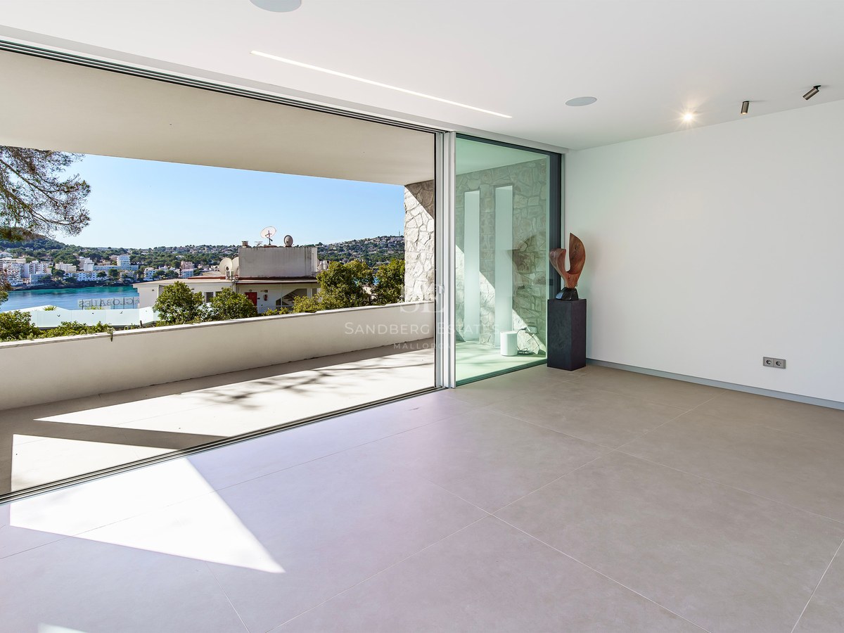 Intérieur minimaliste avec de grandes baies vitrées ouvrant sur une terrasse dominant la côte et la mer.