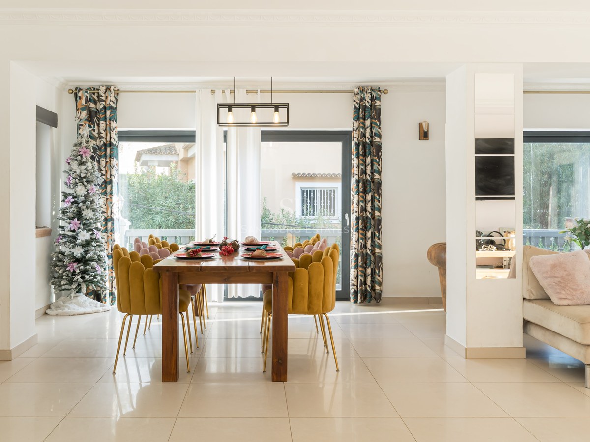 Modern dining area with a large wooden table, mustard velvet chairs, a Christmas tree, and large glass patio doors.