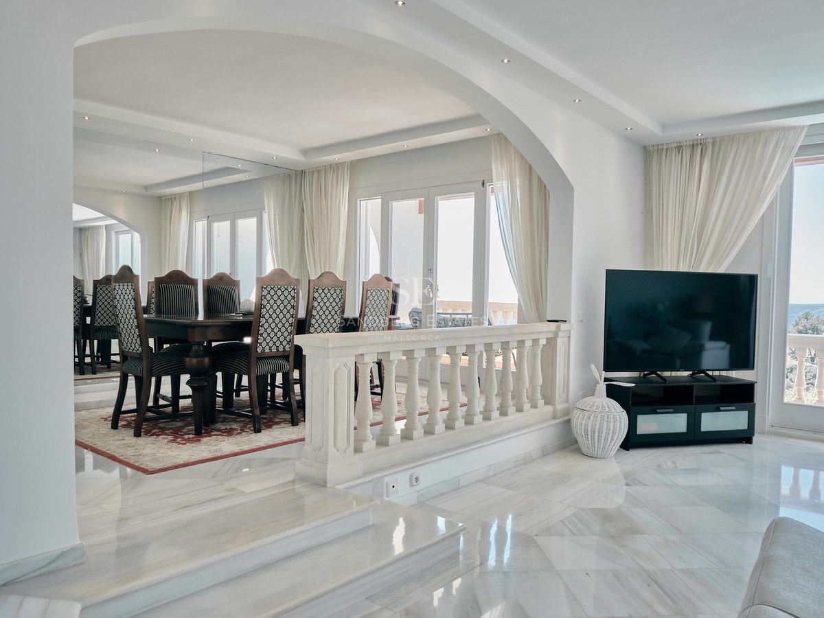 Bright split-level room with polished marble floors, an arched entrance to a dining area, and large terrace windows.