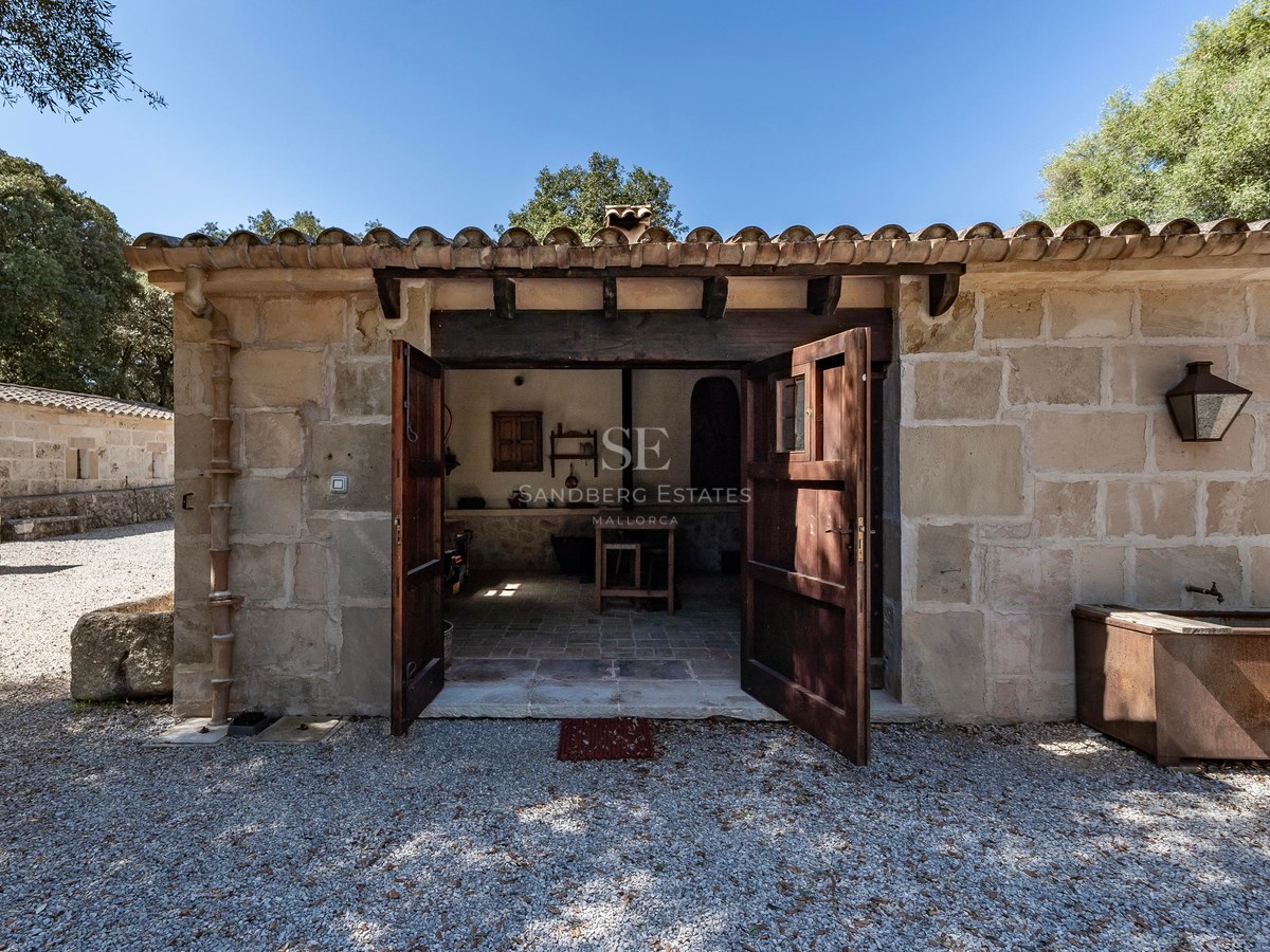 Petit bâtiment rustique en pierre avec portes en bois ouvertes et toit en tuiles sous un soleil radieux.