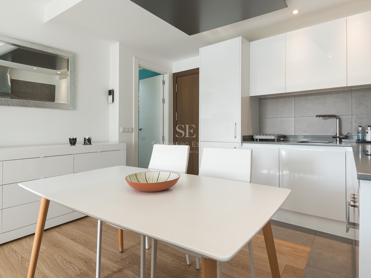 Bright modern kitchen with white cabinetry, a grey backsplash, and a white dining table with wooden legs.