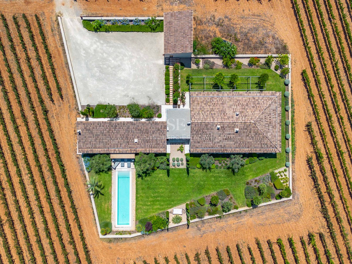 Prise de vue aérienne d'une villa avec piscine turquoise et jardins structurés, entourée de rangées de vignes.