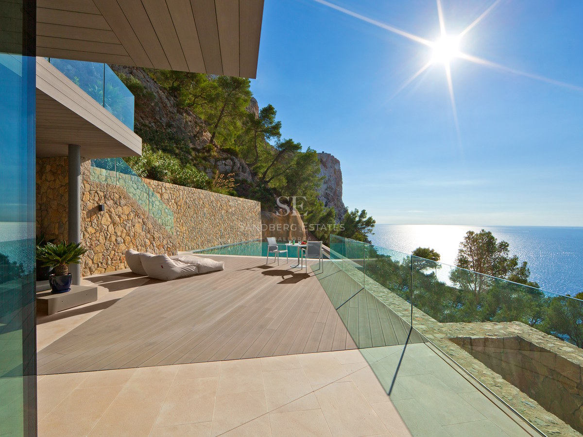 Modern villa terrace with infinity pool, wooden decking, glass railings, and panoramic views of the Mediterranean Sea.