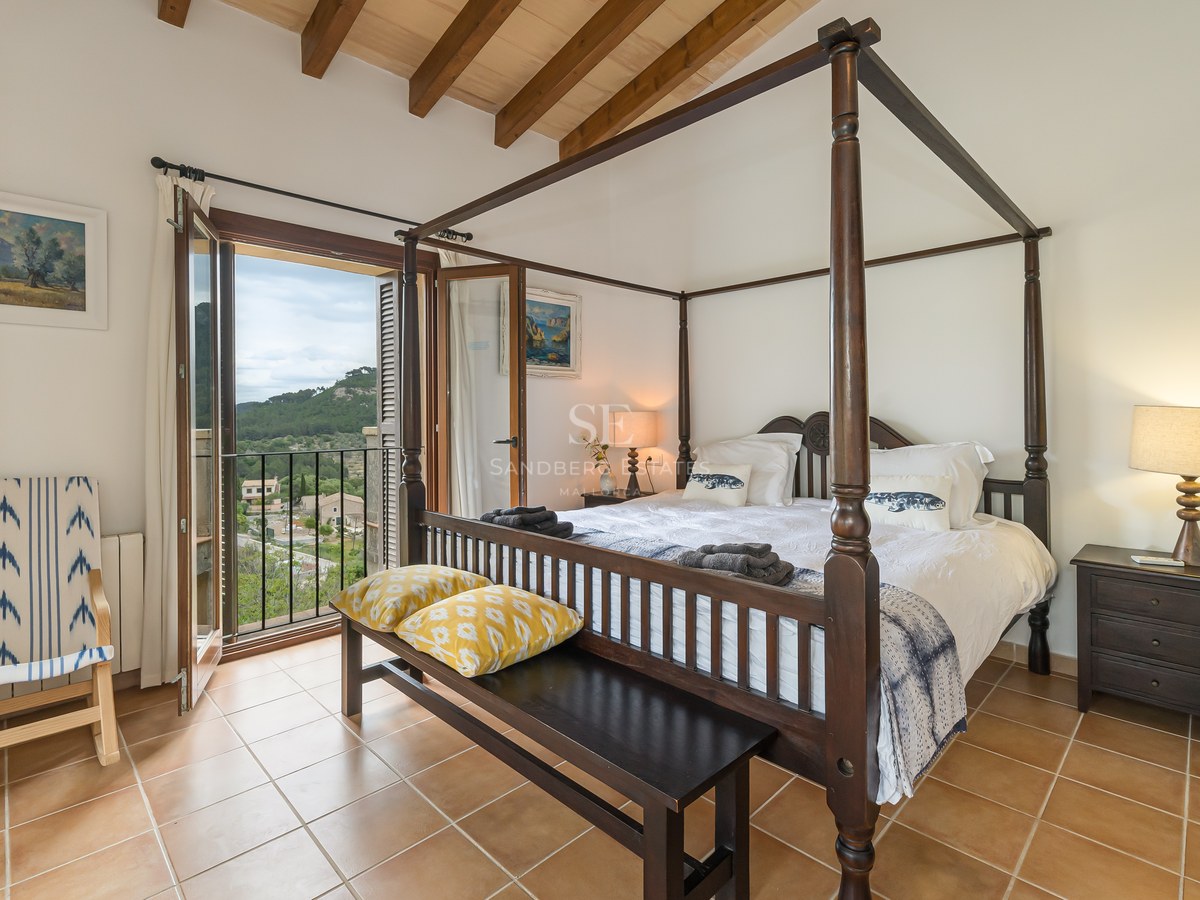 Master bedroom med himmelsäng, träbjälkar, terracottagolv och balkong med utsikt över bergen.