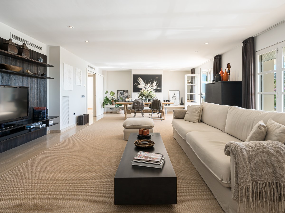 Vaste salon avec canapé beige, meuble multimédia en bois sombre, tapis en fibres naturelles et baies vitrées.