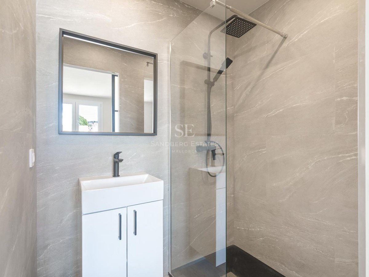 Salle de bains moderne avec carrelage gris effet pierre, paroi de douche en verre et robinetterie noire mate.