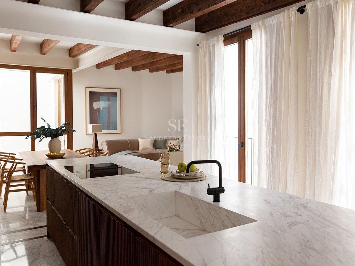 Modern kitchen featuring a white marble island with integrated sink, dark wood cabinetry, and exposed ceiling beams.
