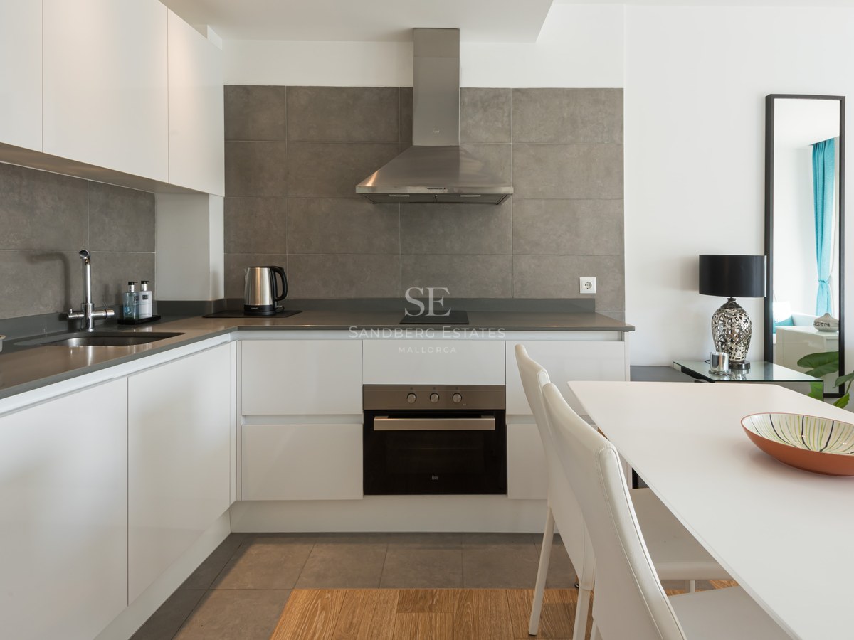 Modern white kitchen with grey tile backsplash, stainless steel appliances, and white dining table.