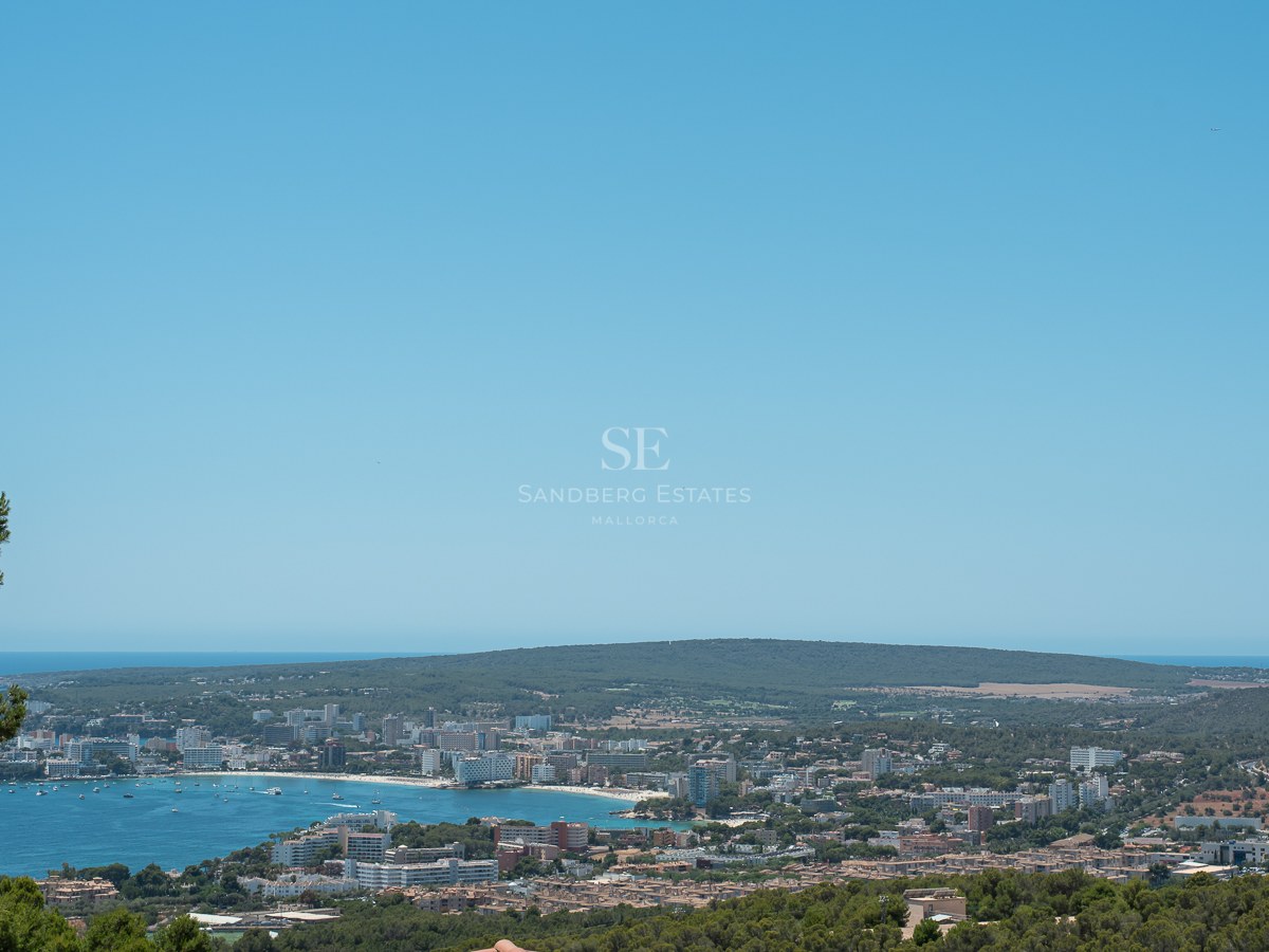 Vue panoramique surélevée d'une baie méditerranéenne bleue, d'une ville côtière et de collines verdoyantes.