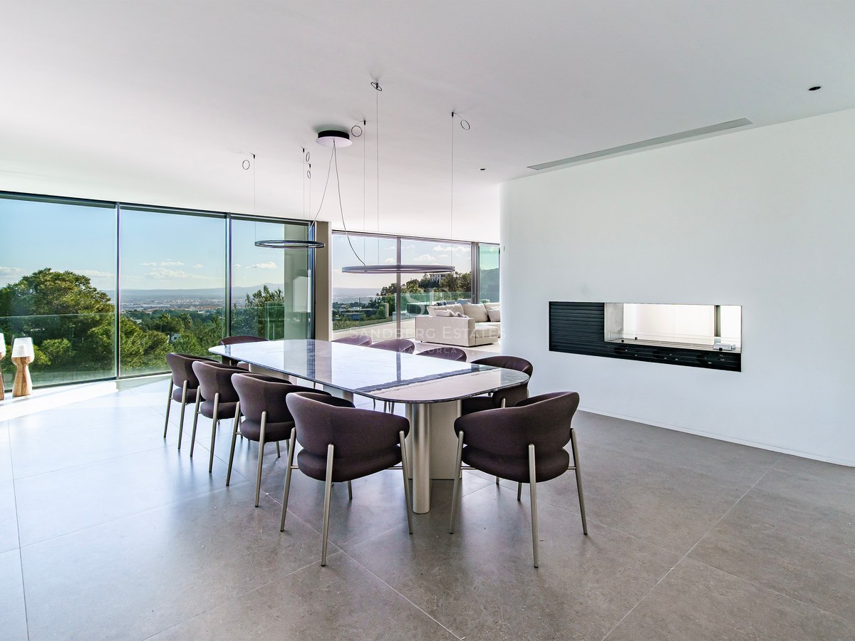 Salle à manger moderne élégante avec une grande table, des chaises sombres et des baies vitrées donnant sur la nature.