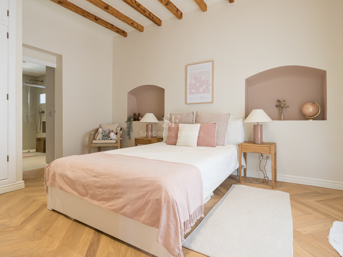 Bright bedroom with herringbone oak floors, wooden ceiling beams, a double bed, and an adjoining ensuite bathroom.