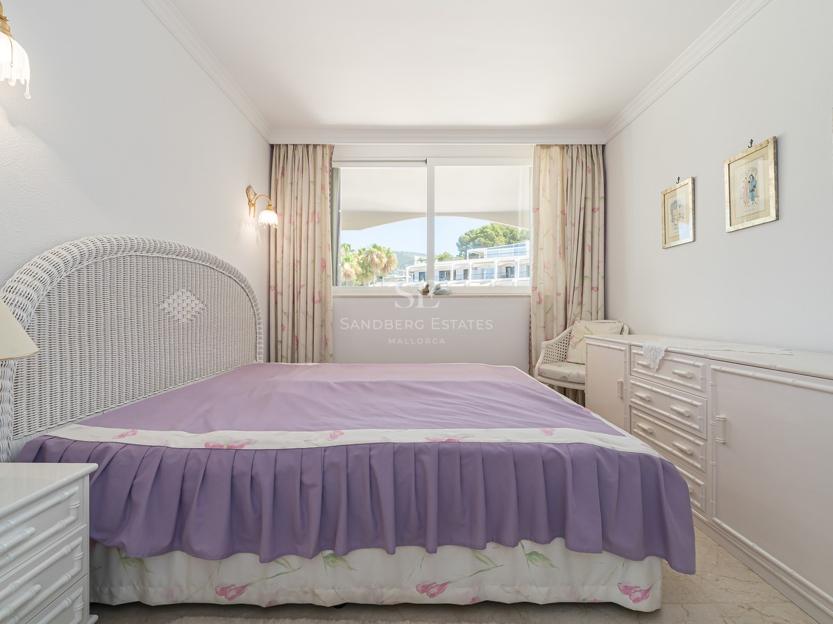 Bedroom featuring a white wicker headboard, purple bedspread, and a large window overlooking a sunny courtyard.