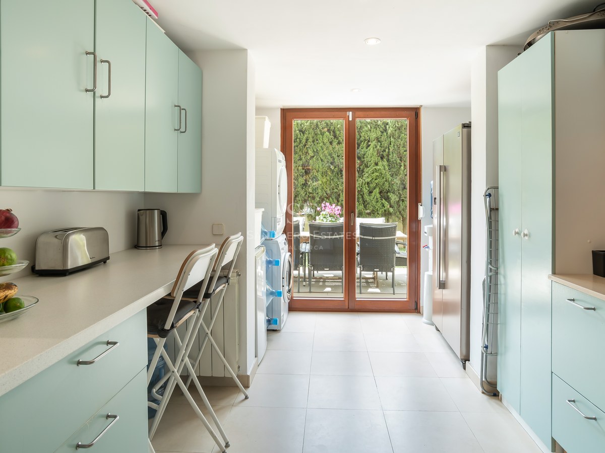 Cocina luminosa con armarios verde menta, encimeras blancas, zona de lavandería y puertas de cristal hacia el patio.