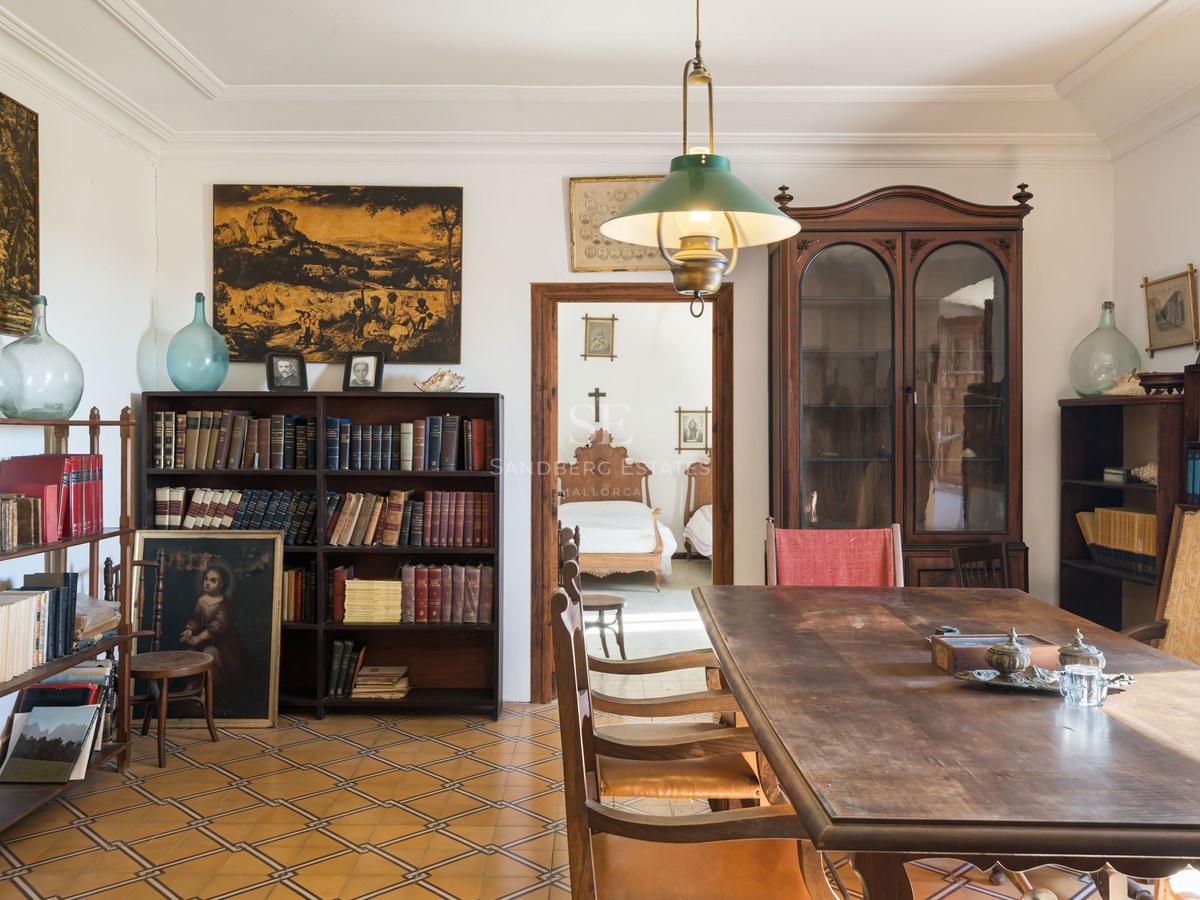 Habitación clásica con gran mesa de madera, estanterías repletas de libros y suelo de baldosas decoradas.