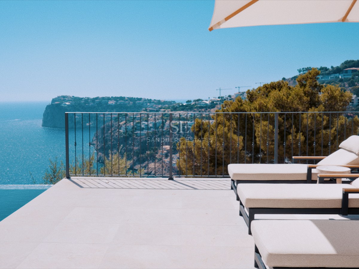 Luxury terrace featuring white sun loungers and a parasol next to an infinity pool overlooking the sea and cliffs.