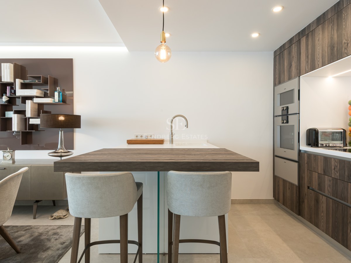 Modern kitchen featuring a dark wood island with grey bar stools, sleek cabinetry, and integrated high-end appliances.