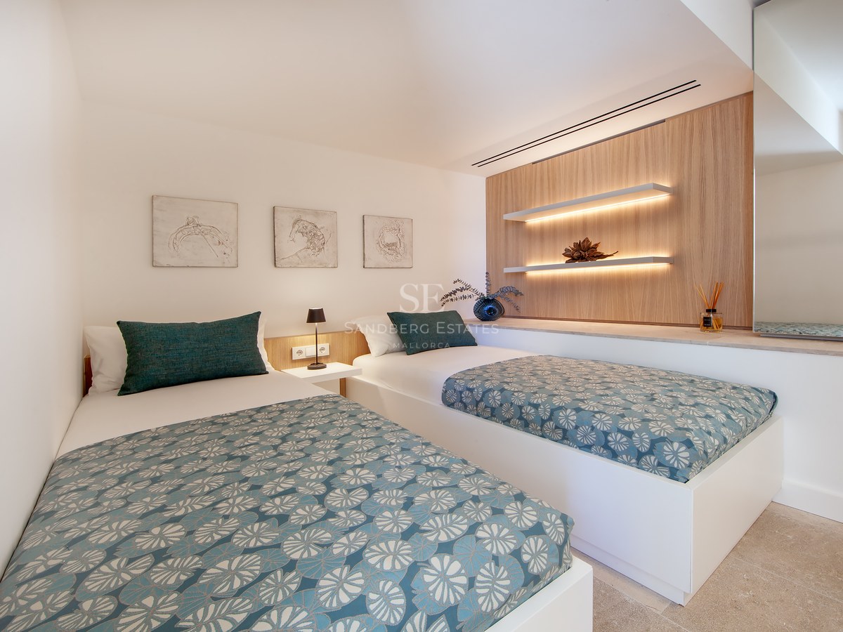 Modern bedroom featuring two single beds with teal patterned covers, wooden wall panels, and warm LED floating shelves.