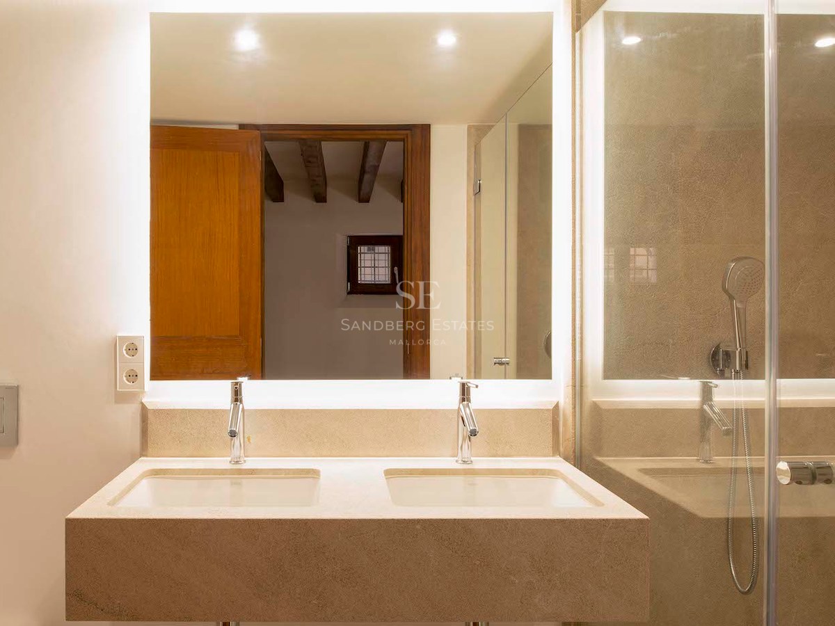 Bathroom with double stone sink, large backlit mirror, and glass shower enclosure.