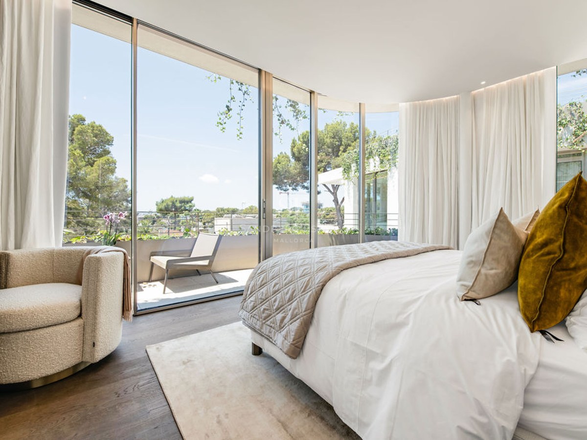 Lyxigt sovrum med fönster från golv till tak, en bouclé-fåtölj och utsikt över en solig privat terrass.