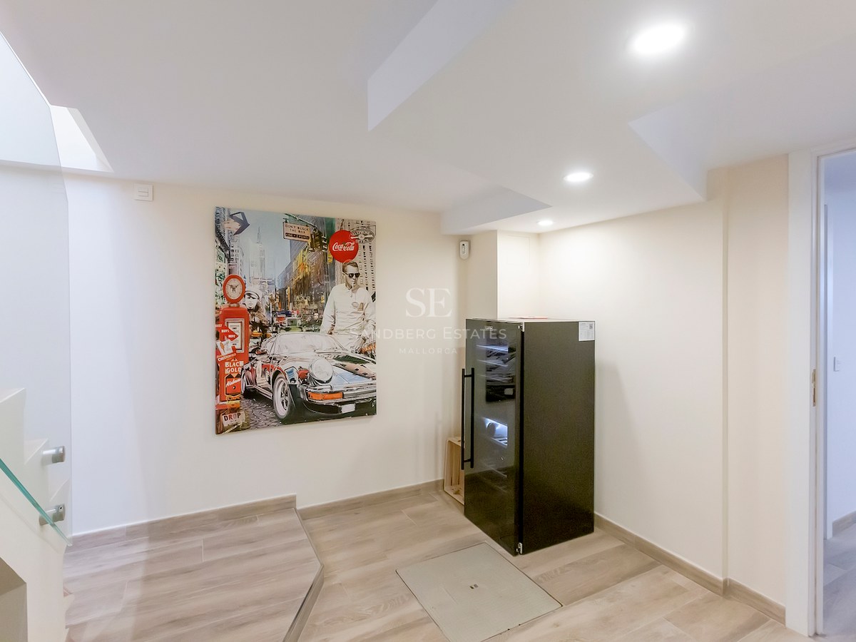 Modern interior landing with a large pop-art painting of a car, a black wine cooler, and glass stairs.